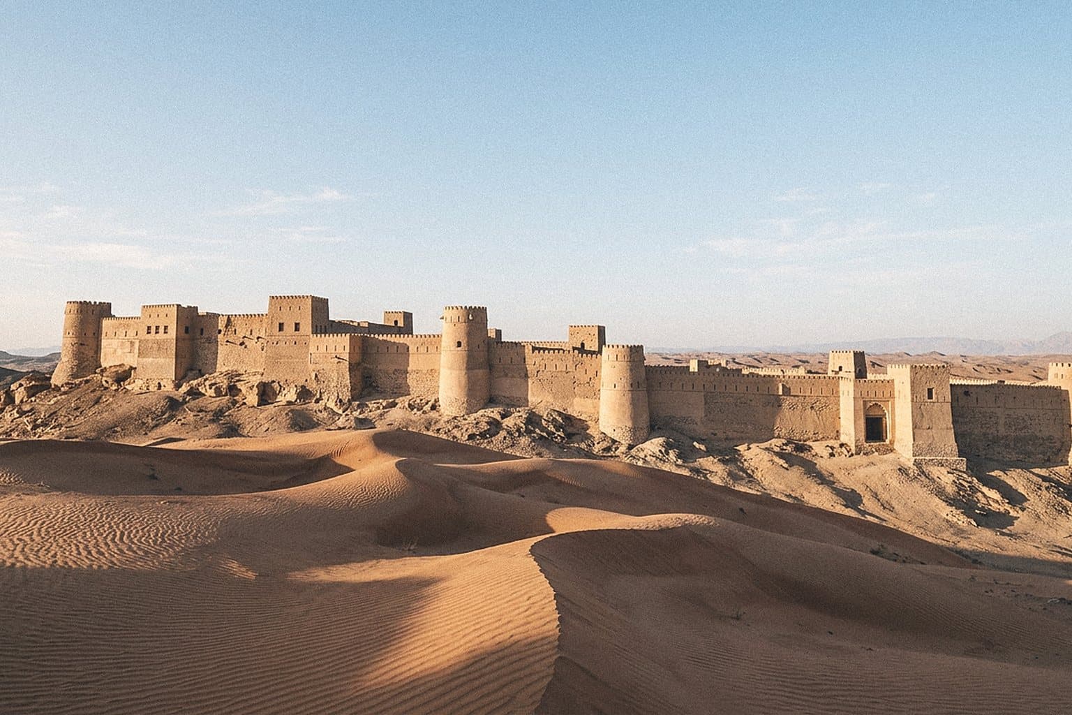 Ancient desert fort wall with towers behind sand dunes