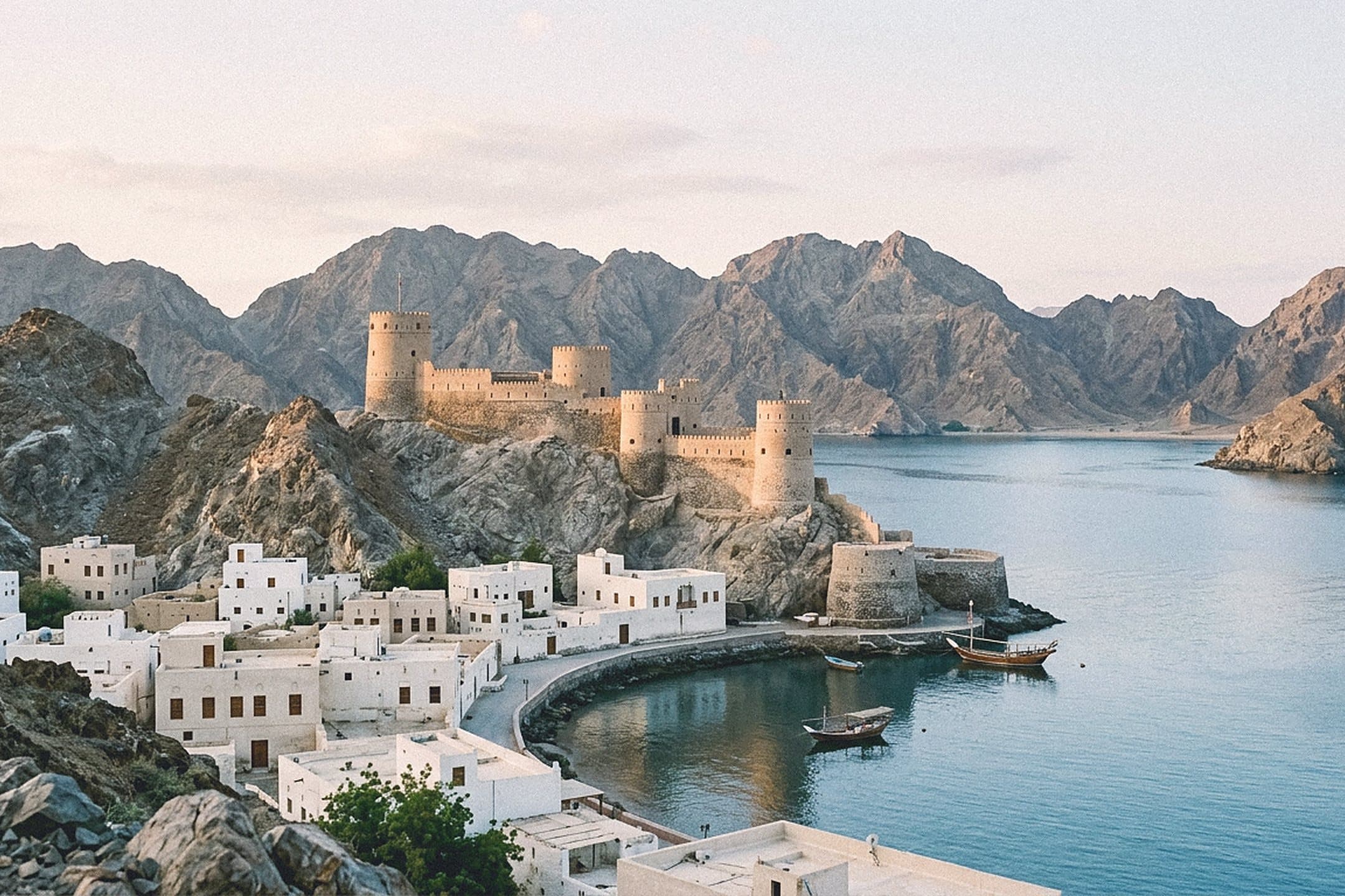 Whitewashed waterfront buildings and an old stone fort on the rocky coast of Muscat