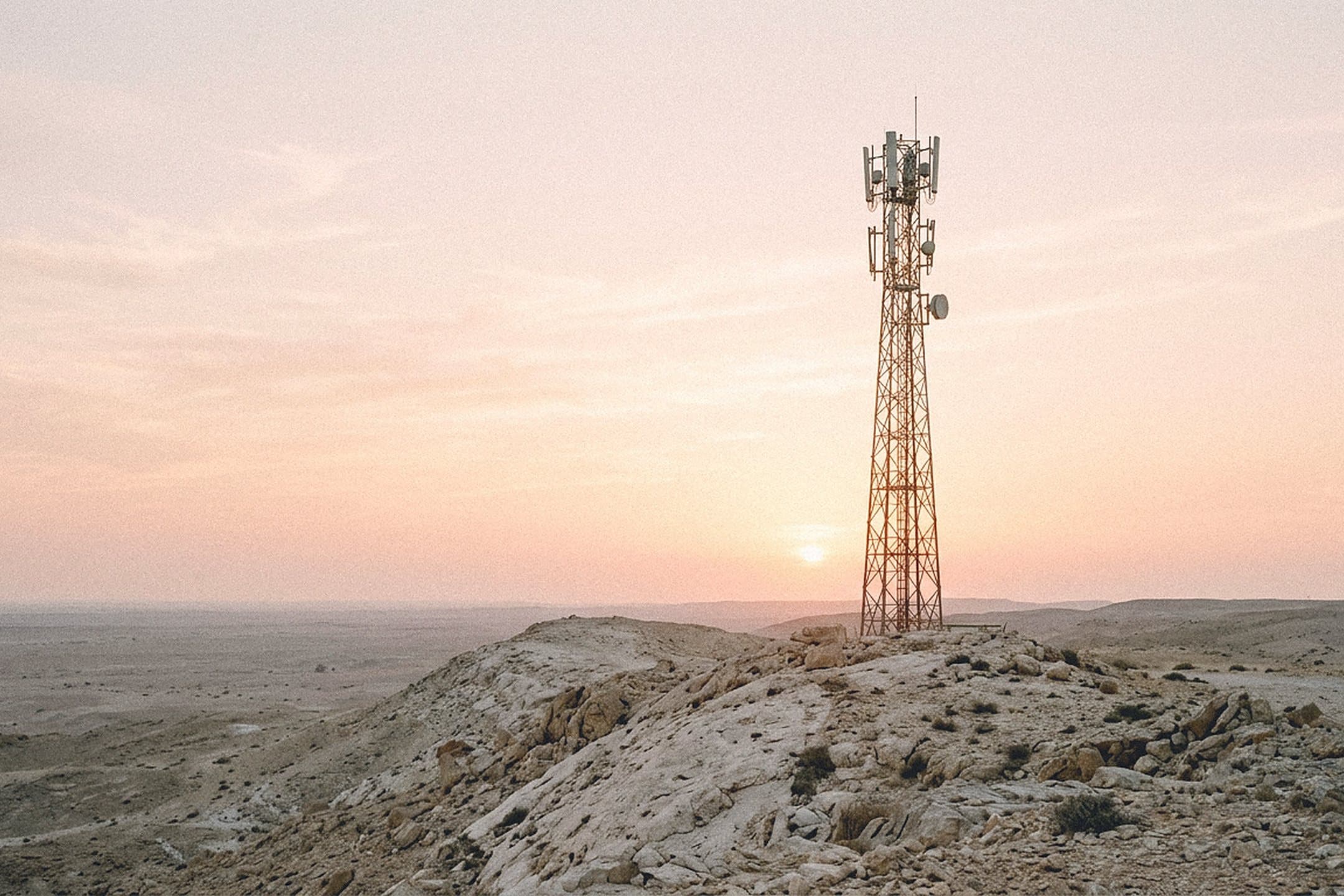 Telecom tower with antenna panels on a rocky desert ridge at dawn