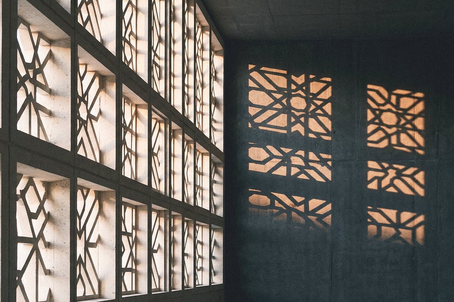 Stone facade with geometric mashrabiya-style perforations casting light patterns
