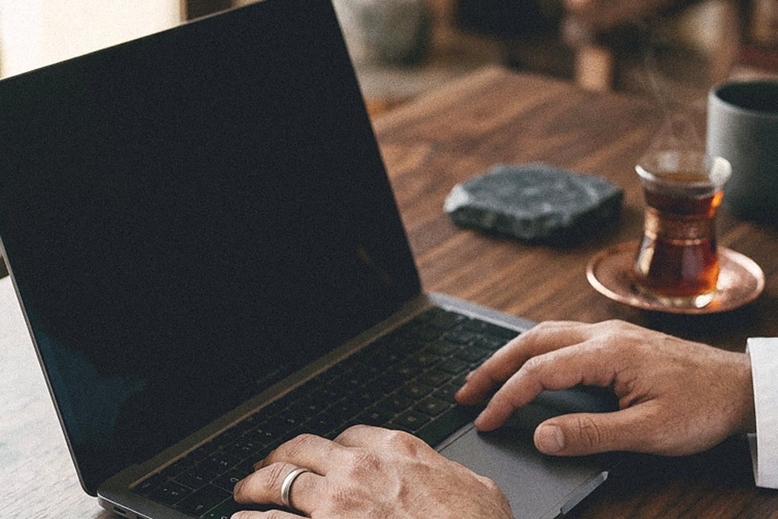 Hands on a laptop keyboard beside a glass of tea on a walnut desk