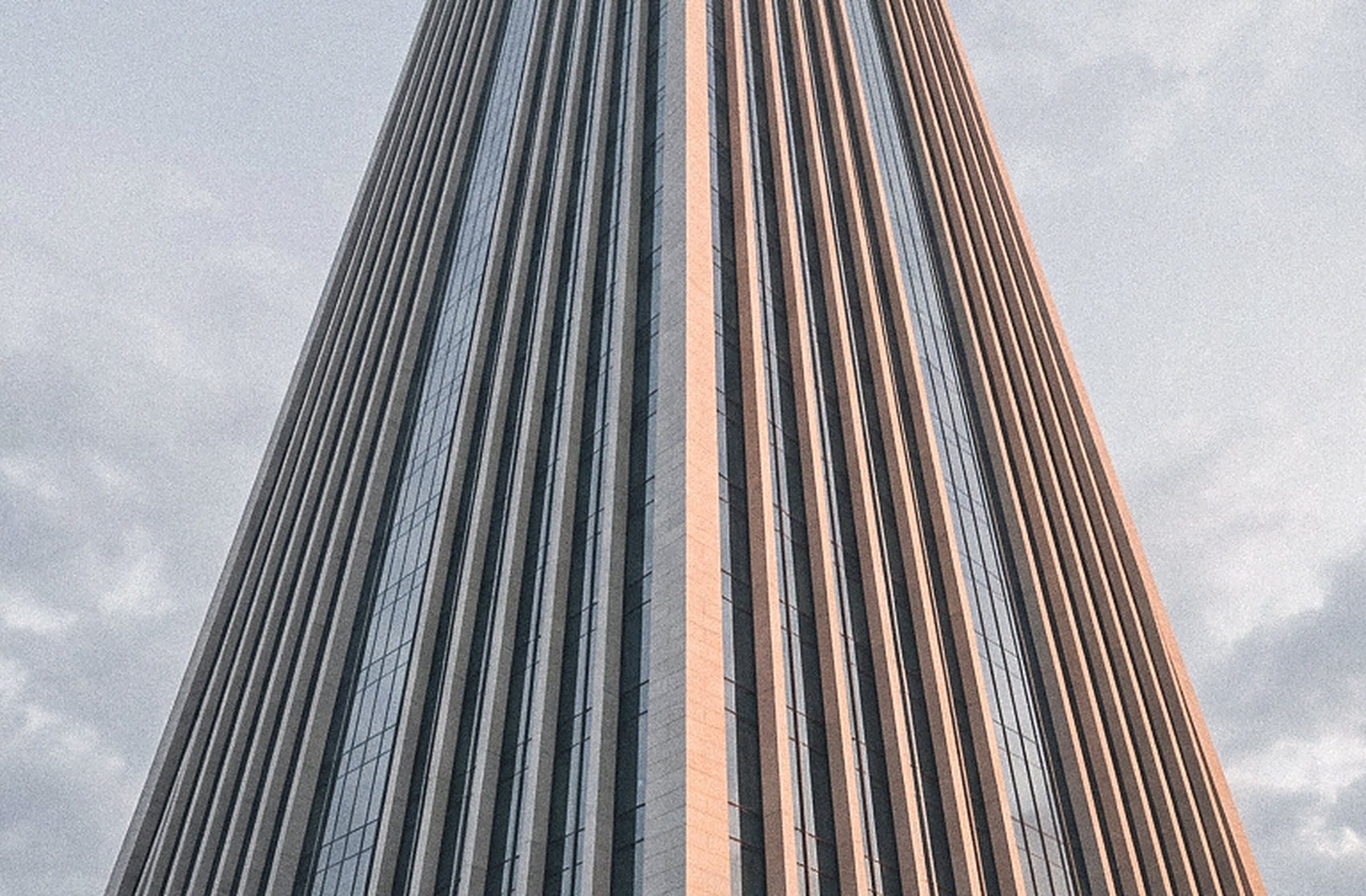 Slender stone-and-glass tower seen from below against a pale sky
