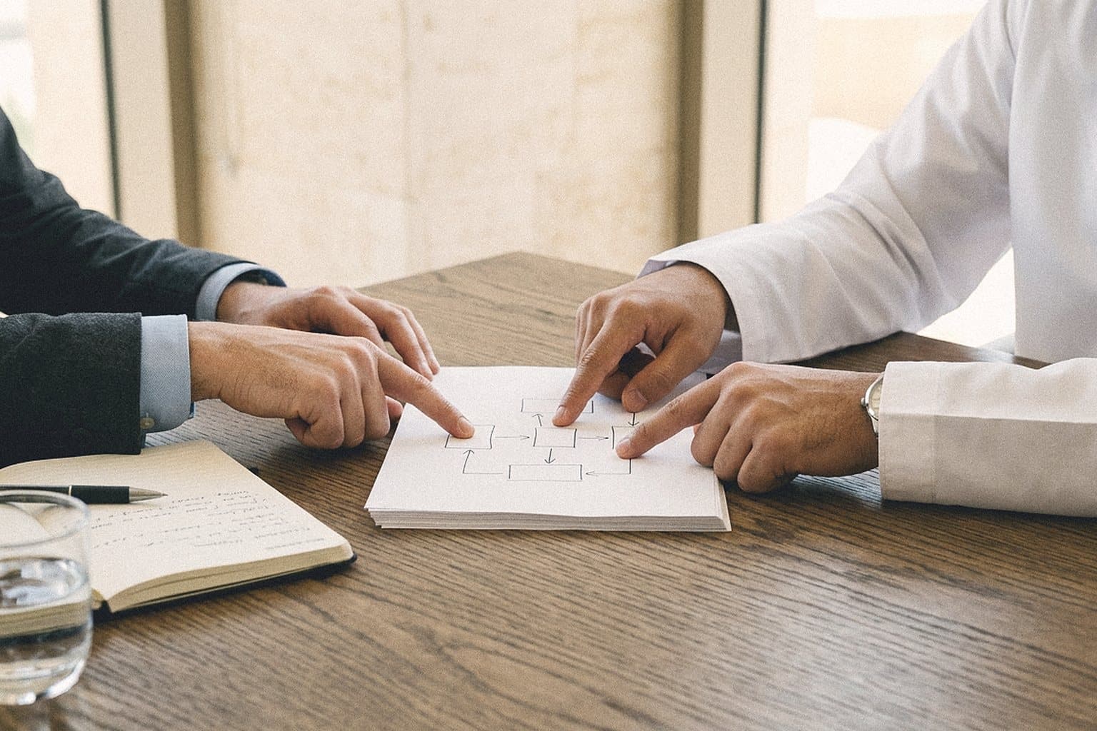 Two people pointing at a printed diagram on a meeting table