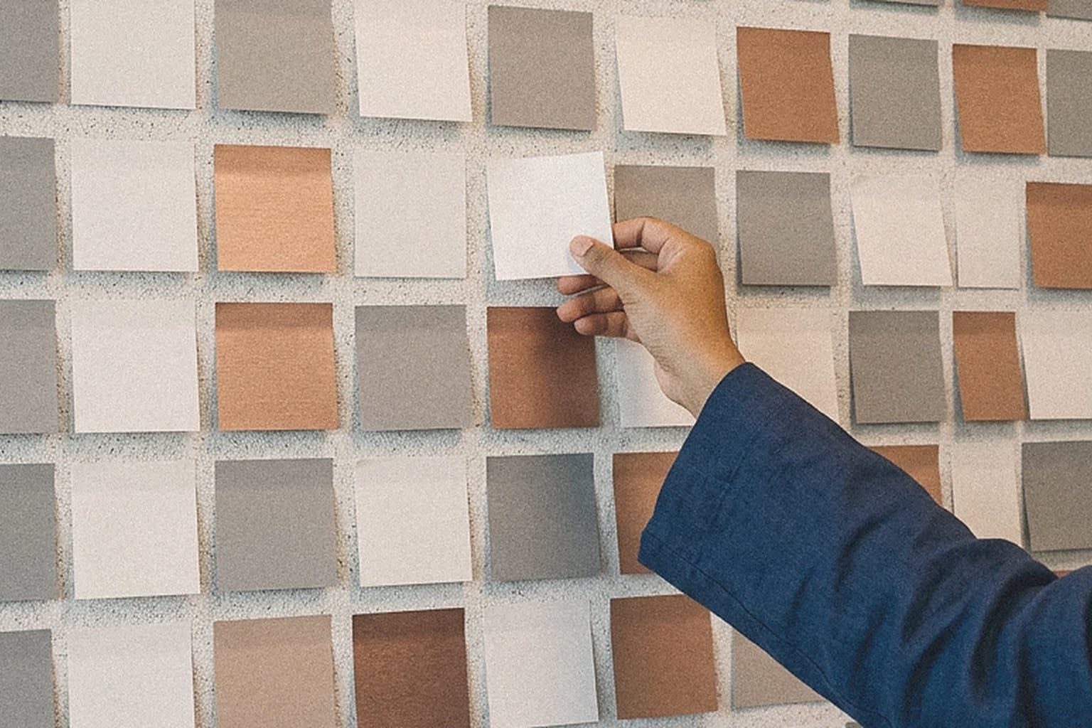 Hand placing a sticky note on a workshop wall of blank notes
